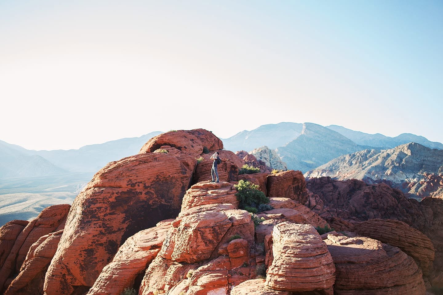 Figure standing atop red rock formations with mountain range behind