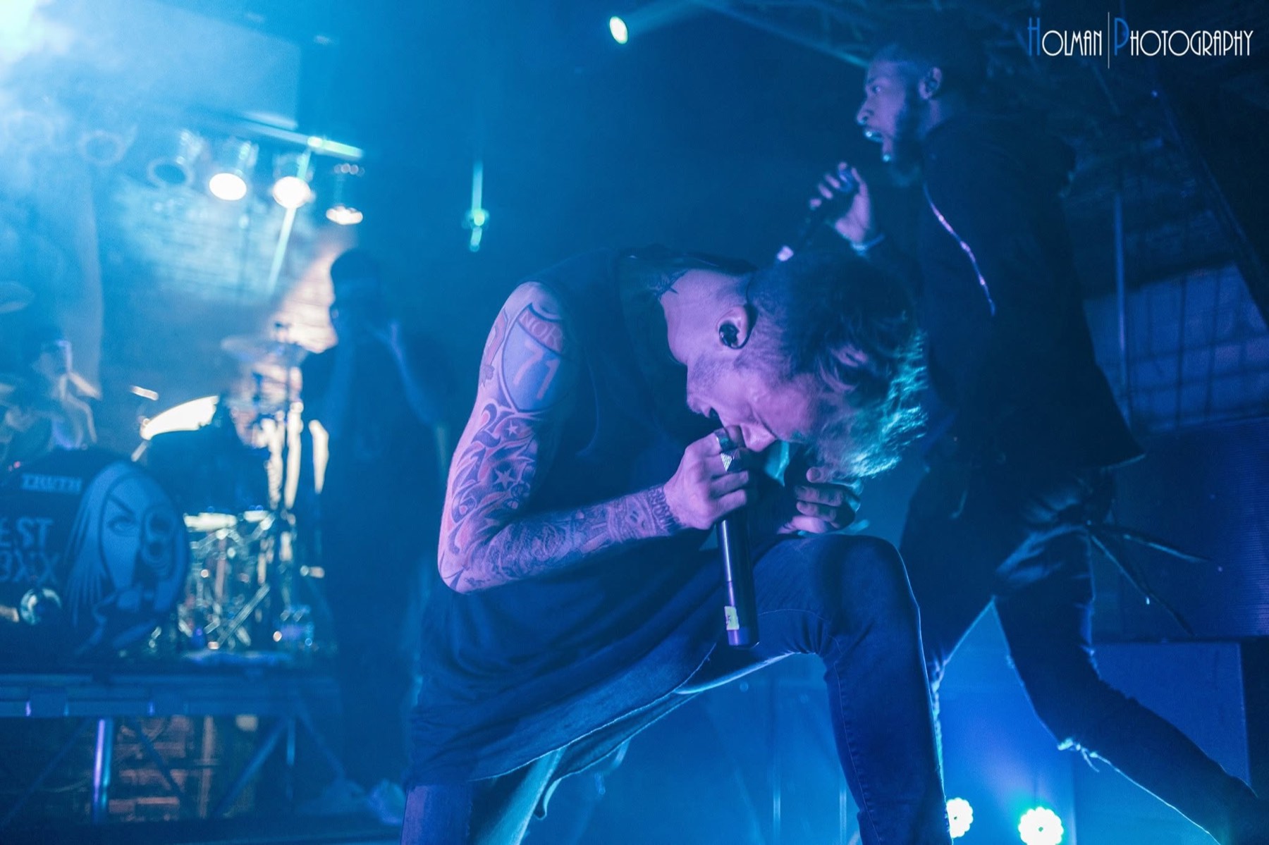 Machine Gun Kelly bent over the microphone in blue stage light