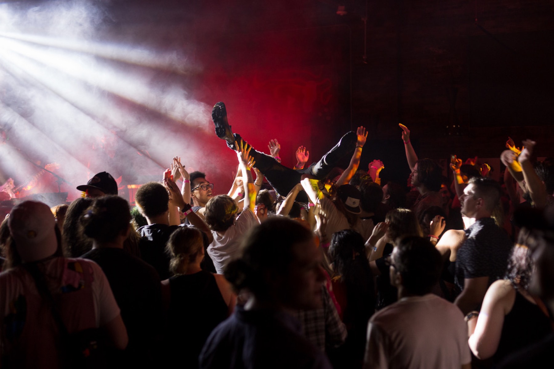 Crowd surfer above a packed floor in stage haze