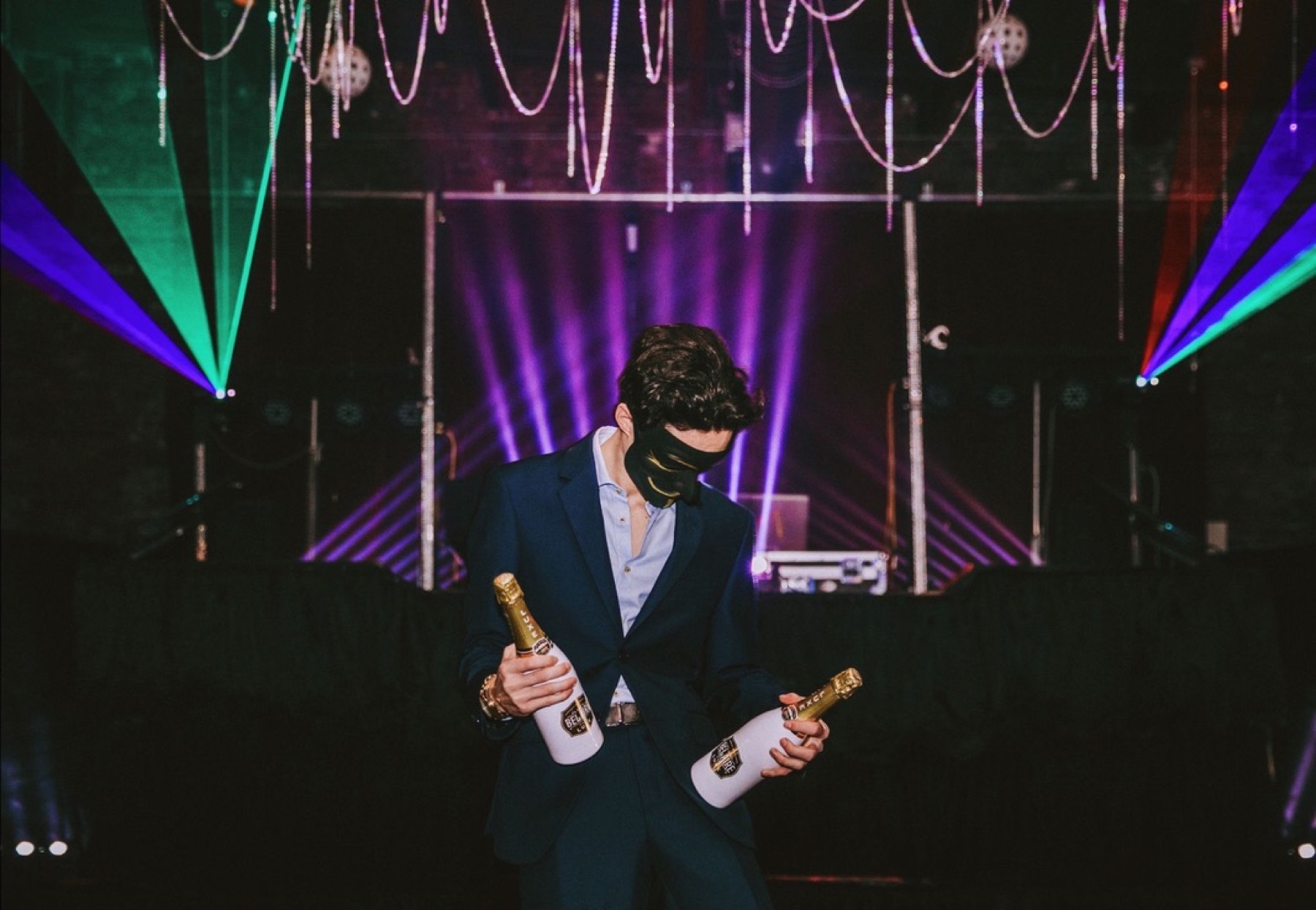 Christian Holman masked in a tuxedo under lasers at a Masquerade Ball